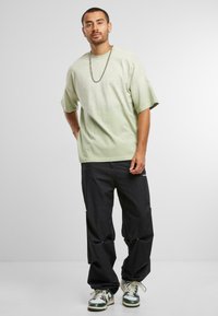 Lys grøn oversized t-shirt med rund hals, sorte cargo bukser og grønne/hvide sneakers, med en kæde halskæde.
