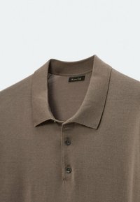 Polo shirt en tricot marron avec un col ribbé, deux boutons noirs et une étiquette visible à l'intérieur du col.