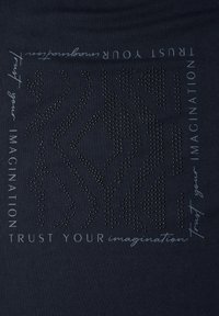 T-shirt navy avec un design texturé de petites clous, portant le slogan "Faites confiance à votre imagination" en texte gris clair contrastant.
