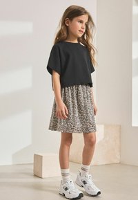 Top corto nero abbinato a una gonna plissettata con stampa leopardata. Indossato con sneakers bianche e calze alla caviglia a righe. Tessuto morbido, design casual.