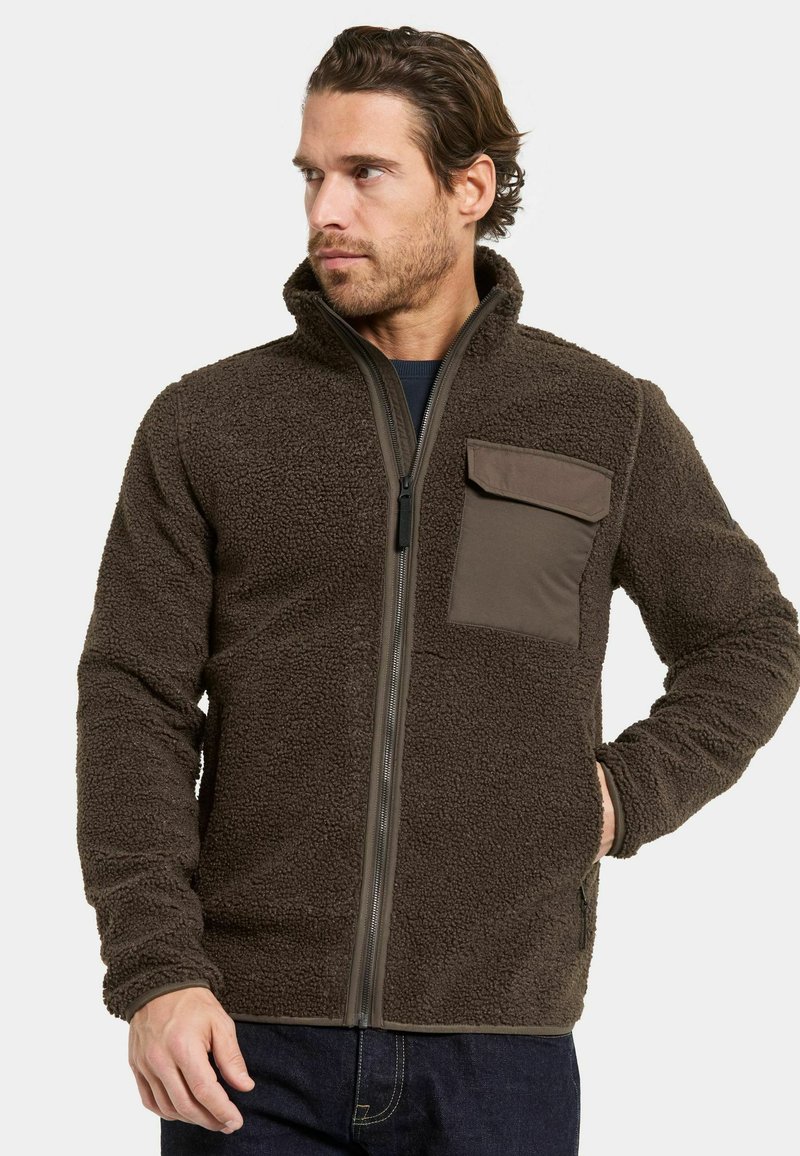 Ruskea fleece-takki, jossa on teksturoitu pinta, täydellinen vetoketju ja rintatasku kontrastiväristä kangasta. Mukana korkea kaulus ja istutetut hihat.