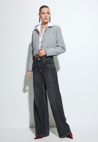 Chaqueta corta gris con un tejido texturizado, cierre de botones, combinada con jeans negros de pierna ancha y tacones rojos de punta. Camisa blanca debajo.
