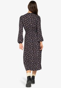 Rochie midi neagră cu flori, cu mâneci lungi, talie strânsă, detalii elastice și modele cu flori mici colorate. Purtată cu cizme negre și șosete albe.