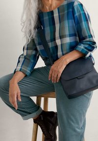 Plaid top in blue and green tones, dark navy crossbody bag, light green corduroy pants, and brown lace-up boots with a matte finish.