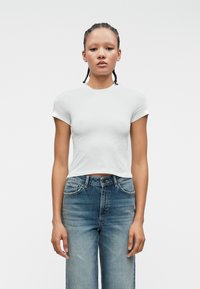 Λευκό cropped μπλουζάκι με κοντά μανίκια συνδυασμένο με ψηλόμεσα ανοιχτόχρωμα μπλε τζιν. Και τα δύο κομμάτια διαθέτουν ένα απλό, καθαρό σχέδιο και ομαλή υφή.