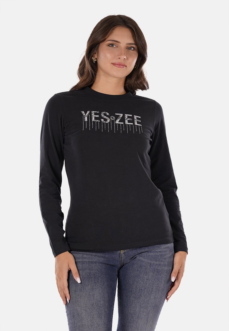 Maglietta nera a maniche lunghe in morbido tessuto con una grafica di strass argentati che riporta la scritta "YES-ZEE" sul fronte. Dettagli includono un collo tondo.