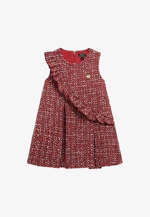 Robe sans manches en tweed rouge et blanc avec une ceinture à volants sur le devant, une jupe plissée et un petit emblème en forme de cœur doré sur la poitrine.
