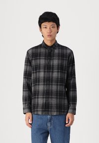 Μαύρο και γκρι καρό πουκάμισο από φλιάνελ ύφασμα, με κουμπωτό μπροστινό μέρος, γιακά και μακριά μανίκια, συνδυασμένο με μπλε τζιν παντελόνι.