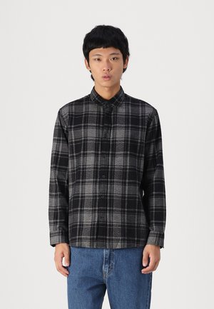 Zwart-grijze geruite flanellen blouse met knoopsluiting aan de voorkant, kraag en lange mouwen, gedragen met blauwe denim jeans.