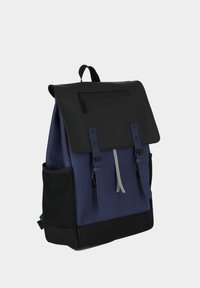 Zaino blu navy con pattina nera, dotato di una tasca frontale con zip, due cinghie con fibbie e tasche laterali in rete. Materiali texturizzati e resistenti.