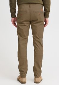 Khaki bavlněné chinos s dvěma zadními kapsami, viditelným šitím a hnědými knoflíky. Hladká textura, rovný střih a jemný branding.