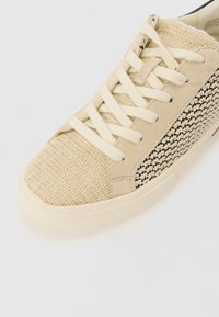 Sneaker beige con dettagli in tessuto intrecciato e finiture in suede liscio. Presentano lacci piatti color avorio e una suola in gomma texturizzata.