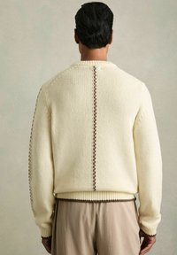 Krēmkrāsas adīts džemperis ar ribotu apakšmalu un aprocēm, ar brūnu izšuvumu pa aizmuguri un plecu šuvēm.