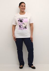 White cotton t-shirt featuring a floral graphic in black and pink, with the word "FRESHNESS" above. Paired with dark blue jeans and black flats.