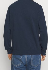 Mörkblå sweatshirt med långa ärmar, ribbade muddar och nederkant. Mjukt bomullsblandat material, minimalistisk design utan synliga logotyper eller mönster.