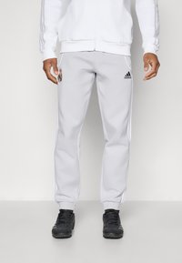 Pantaloni sportivi grigi in una vestibilità rilassata, con strisce bianche ai lati, un patch con logo e polsini elastici. Abbinati a scarpe da ginnastica nere.