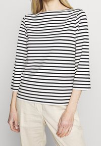 Black and white striped long-sleeve top with a boat neckline, made from soft fabric, paired with cream-colored linen trousers.