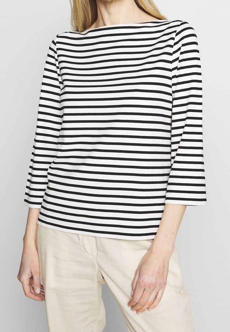 Black and white striped long-sleeve top with a boat neckline, made from soft fabric, paired with cream-colored linen trousers.