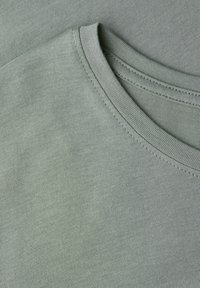 Zielona bawełniana koszulka z okrągłym dekoltem, gładką fakturą i widocznymi detalami przeszyć. Tkanina wydaje się miękka i lekka.