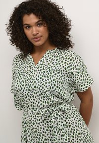 Vestido de manga corta en tela blanca con puntos verdes y azules marinos. Escote en V y detalle de cintura atada. Material ligero y texturizado.