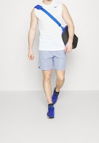 Camiseta deportiva blanca sin mangas, pantalones cortos azul claro, zapatos deportivos azules y un bolso negro con detalles azules, con un diseño cruzado.