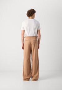 Pantalones de pierna ancha color beige con una textura suave, con un frente liso y bolsillos traseros. Combinados con una camisa blanca de manga corta.
