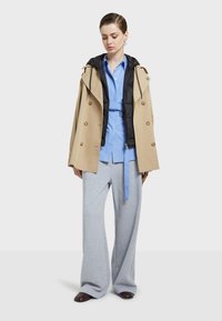 Beige kaksareggsjakke med svart indre lag, lyseblå skjorte, grå vide joggebukser og mørke sko.