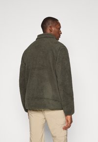 Dunkelgr�üne Fleecejacke mit hohem Kragen, strukturiertem Material und langen Ärmeln. Hat einen lockeren Schnitt und keine sichtbaren Metallteile.