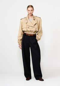 Beež kärbitud nõelrõivas, millel on elastne vöökoht, suured nupud ja õlavarre kaitsed, koos kõrge vöökohaga mustade pükste ja pruuni nahkvöötmega.