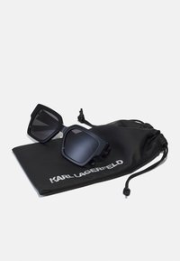 Occhiali da sole neri con montatura quadrata oversized, dotati di lenti scure. Accompagnati da un sacchetto con coulisse nero con il logo bianco "KARL LAGERFELD".
