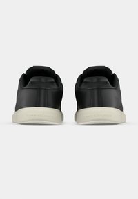 Adidași negri din piele cu textură netedă, formă rotunjită și talpă albă contrastantă, având un logo discret pe călcâi.