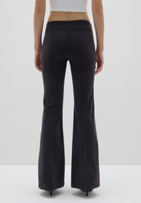 Schwarze, ausgestellte Hosen mit einer glatten Textur, die einen hohen Bund und sichtbare Nähdetails entlang der Nähte aufweisen.