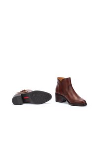 Botas de tobillo de cuero marrón con tacón bajo, puntera redondeada, recortes laterales y una suela de goma texturizada con un patrón de estrellas.