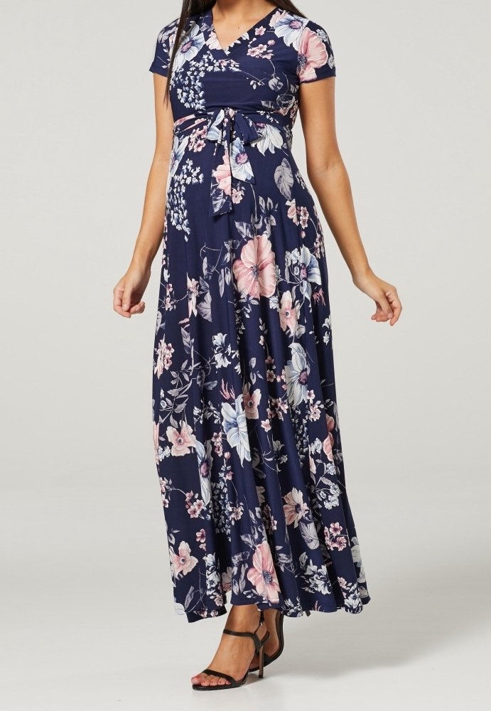 Woman wearing a navy blue floral wrap maxi dress with short sleeves and a tied waist, paired with black high-heeled sandals.