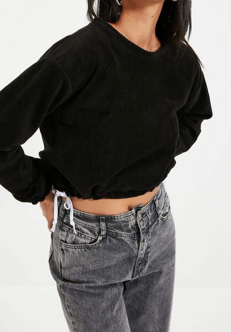 Felpa nera corta realizzata in morbido tessuto, con maniche lunghe e orlo con cordino, abbinata a jeans grigi a vita alta con dettagli sbiaditi.