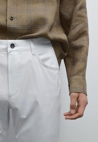Witte katoenen broek met voorzakken en een knoopsluiting, gecombineerd met een bruine geruite overhemden met knopen van een gestructureerde stof.