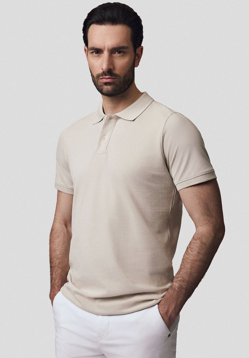 Beżowa koszulka polo z krótkimi rękawami, miękka w dotyku, z zapięciem na trzy guziki i klasycznym kołnierzykiem, sparowana z białymi spodniami.