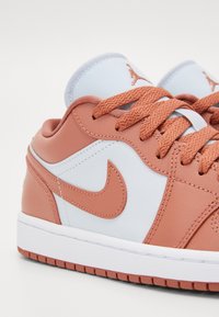 Gros plan sur une basket Nike beige et blanche avec des lacets texturés et un logo visible sur le côté et la languette.