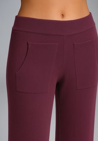 Leggings bordeaux con una consistenza morbida, dotati di una cintura ampia e due tasche frontali. Il design è aderente e liscio.