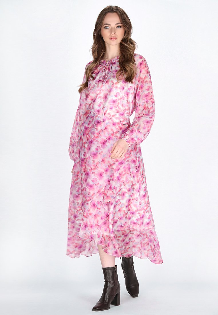Langes pinkes Kleid mit floralen Mustern, aus leichtem Stoff gefertigt. Verfügt über einen gerafften Ausschnitt und lange, durchsichtige Ärmel. Braune Knöchelstiefel.