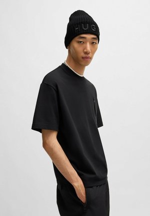Svart t-skjorte med korte ermer, minimalistisk design og lomme, sammen med en ribbet svart lue med ordet "HUGO."