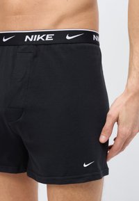 Ανδρικός κορμός με μαύρα μποξεράκια Nike με λογότυπο στη μέση και μικρό λευκό σήμα Nike κοντά στο τελείωμα.