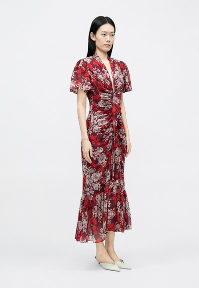 Vestido floral vermelho com tecido transparente, design franzido, mangas curtas bufantes e barra rodada. Combinado com sapatilhas pontiagudas de cor clara.