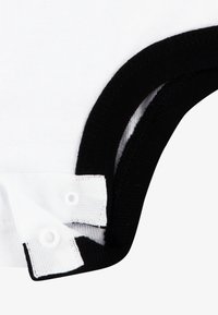 Peça de algodão a preto e branco com decote redondo, com acabamento canelado preto e fechos de pressão brancos na lateral. Textura suave.