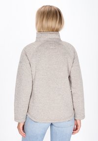 Lichtbeige pullover met een hoge kraag, een gladde textuur en raglanmouwen. Heeft een ontspannen pasvorm en een subtiel gemêleerd patroon.