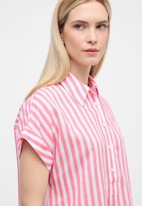 Camicia a maniche corte con bottoni, caratterizzata da strisce verticali alternate rosa e bianche, realizzata in tessuto leggero con una texture morbida.