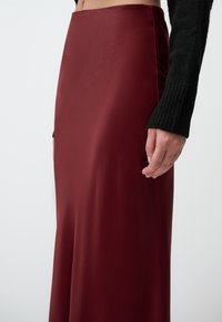 Gonna in satin bordeaux, lunga fino al pavimento con una texture liscia e vita aderente. Abbinata a un maglione in maglia a coste nero sulla parte superiore.