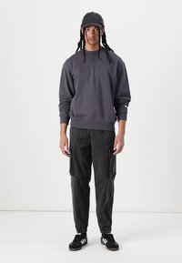 Grå sweatshirt, svarta cargobyxor med fickor, svart keps och svarta sneakers. Avslappnad streetwear-stil. Justerbara ärmslut och midja.