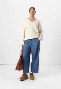 Light beige textured knit sweater with a V-neck, paired with wide-legged blue denim trousers. Brown leather shoulder bag and brown platform shoes.