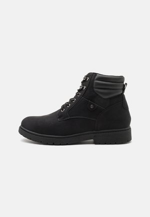Bottine noire avec lacets à l'avant, col rembourré, détail bouton latéral et semelle en caoutchouc texturée sur fond blanc.